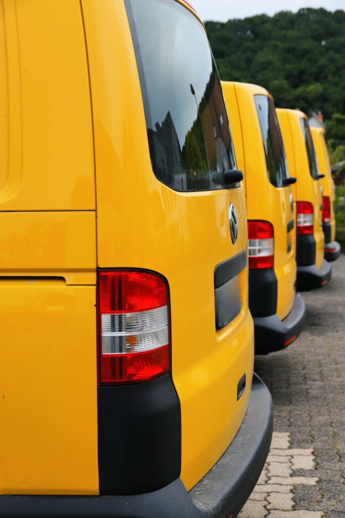 Bright yellow vans aligned in a parking lot outdoors, with lush greenery in the background.
